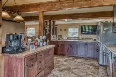 Start your morning right at our dedicated Coffee Bar! This central island features a coffee maker, mugs, and supplies. Rustic wood beams and warm cabinetry define this open kitchen, which looks into the cozy main living room.
