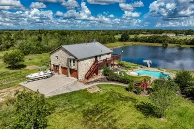 This stunning aerial view highlights the entire property: the handsome stone home with a two-car garage, large driveway (perfect for boat parking), private swimming pool, and a stocked pond with its own pier. Enjoy the complete 5-acre retreat!