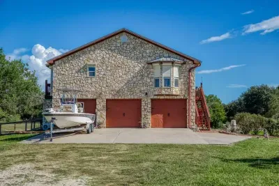 The front of the home features a beautiful stone facade and a two-car garage with charming wood-tone doors. The large driveway and yard offer plenty of space for parking, including a boat (seen here) or other recreation vehicles.
