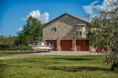 The front of the home features a beautiful stone facade and a two-car garage with charming wood-tone doors. The large driveway and yard offer plenty of space for parking, including a boat (seen here) or other recreation vehicles.