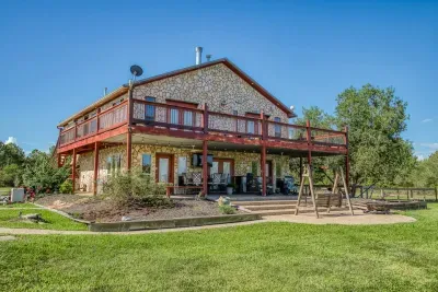 The grand exterior of your retreat! The home features beautiful stone siding, a huge two-level deck, and a covered patio below. The spacious yard offers outdoor seating and a swing set for enjoying the Texas sun.