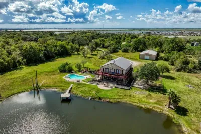 Experience the full 5-acre retreat! This aerial view showcases the stone home, private pool, large deck, fishing pond with a pier, and the spacious grounds. In the distance, enjoy views of the bay and surrounding area.