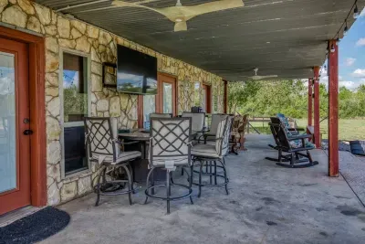 Enjoy the great outdoors from the covered patio! It features a bar-height dining set for meals, comfortable rocking chairs for relaxing, and a large outdoor TV - all against the home's rustic stone wall. Two powerful ceiling fans keep you cool.