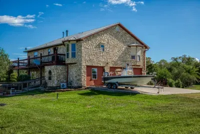 The front of the home features a beautiful stone facade and a two-car garage with charming wood-tone doors. The large driveway and yard offer plenty of space for parking, including a boat (seen here) or other recreation vehicles.