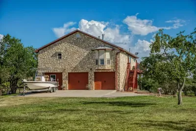 The front of the home features a beautiful stone facade and a two-car garage with charming wood-tone doors. The large driveway and yard offer plenty of space for parking, including a boat (seen here) or other recreation vehicles.