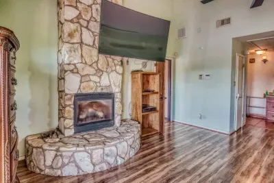 The luxurious master bedroom features a floor-to-ceiling stone fireplace with a raised hearth. Above the rustic mantel is a large flat-screen TV for evening viewing. Wood-look flooring & a convenient media cabinet complete this cozy retreat.