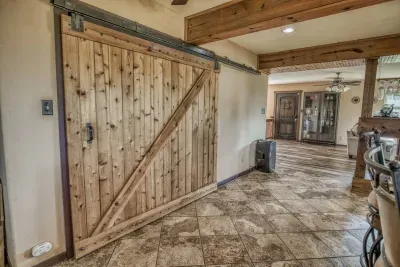 Welcome inside! This image highlights the home's rustic modern style with a beautiful natural wood barn door set against tile flooring. Note the exposed wooden beams and the warm, inviting feel of the entryway.