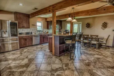 The fully equipped kitchen connects to the dining area. Enjoy meals at the eight-seat dining table or at the granite-top island bar. Features include stainless steel appliances, warm wood cabinetry, and decorative rustic wood beams throughout.