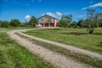 Welcome to the retreat! A long gravel driveway leads through the large, open grassy yard toward the handsome stone-clad house. The front offers a two-car garage and plenty of open space for parking extra vehicles.