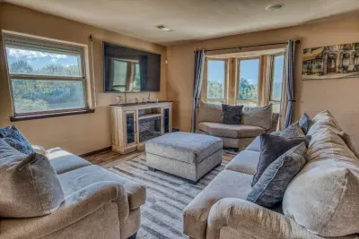 Unwind in this spacious living room featuring plush sectional seating, a large Smart TV over an electric fireplace, and a charming bay window offering serene views. Perfect for relaxing with loved ones after a day of fun.