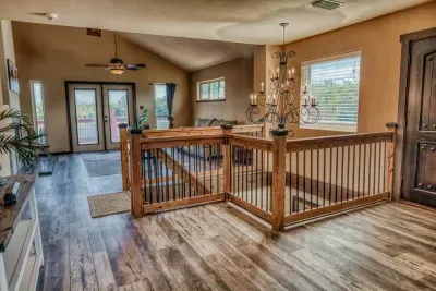 Step into a dramatic entryway, featuring a gorgeous chandelier & rustic-chic wooden stair railings. The wood-look flooring extends into the upstairs living area with French doors that open to the outdoor deck, bathing the space in natural light.