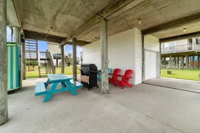 Ground level includes a concrete slab, picnic table, and gas propane grill.  There is two outdoor showers on the left of this picture.  