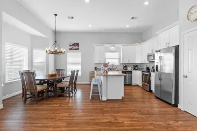 Gather and create in this bright, open kitchen boasting sleek white cabinets, stainless steel appliances, and a beautiful granite island. Adjacent, a charming dining area with a rustic chandelier invites memorable meals on warm hardwood floors.