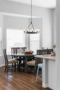 Enjoy sunlit meals at this charming dining nook, featuring a beautiful dark wood round table, comfortable high-back chairs, and a rustic chandelier, all reinforcing the cozy, beach home feel.