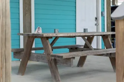Enjoy casual meals outdoors at this rustic wooden picnic table! Located on the covered patio against the vibrant turquoise siding, this outdoor dining area is perfect for family gatherings right near the lower entrance.