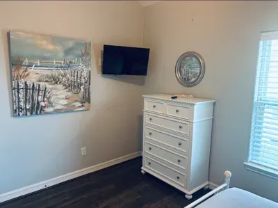 Bright, coastal-inspired bedroom with a calming, airy feel. Features a comfortable bed, spacious dresser, and wall-mounted TV. A simple, clean retreat perfect for relaxing after a day out.