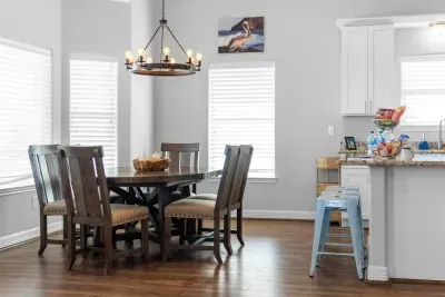 Enjoy sunlit meals at this charming dining nook, featuring a beautiful dark wood round table, comfortable high-back chairs, and a rustic chandelier, all reinforcing the cozy, beach home feel.