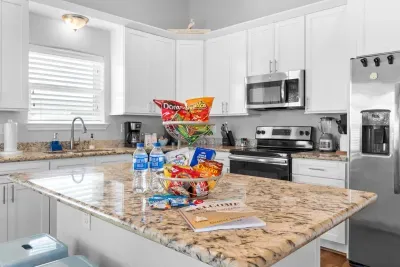 Feel instantly welcomed by this bright kitchen featuring sleek white cabinets, stainless steel appliances, and a beautiful granite island, thoughtfully stocked with complimentary snacks. It's perfectly ready for your vacation enjoyment.