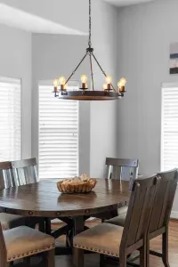 Enjoy sunlit meals at this charming dining nook, featuring a beautiful dark wood round table, comfortable high-back chairs, and a rustic chandelier, all reinforcing the cozy, beach home feel.
