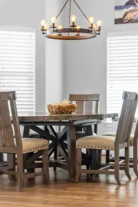 Enjoy sunlit meals at this charming dining nook, featuring a beautiful dark wood round table, comfortable high-back chairs, and a rustic chandelier, all reinforcing the cozy, beach home feel.