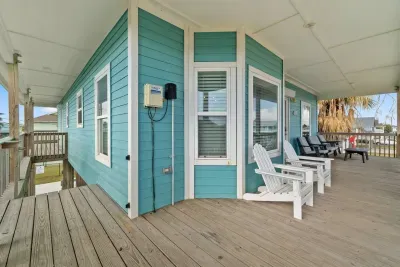 This elevated Upper Deck/Balcony provides a large wooden outdoor space with comfortable seating, including Adirondack chairs and cushioned sofas, perfect for enjoying the coastal air and neighborhood views.