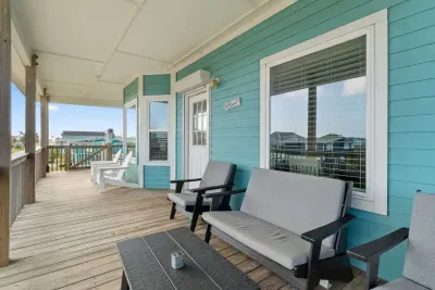 Enjoy beautiful views from the Upper Deck/Balcony! This raised wooden deck features stylish gray cushioned sofas and a table, perfect for relaxing in comfort and enjoying the coastal air.