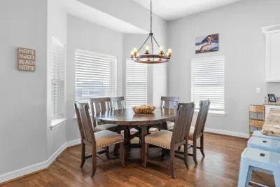 Enjoy sunlit meals at this charming dining nook, featuring a beautiful dark wood round table, comfortable high-back chairs, and a rustic chandelier, all reinforcing the cozy, beach home feel.