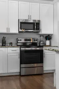 This bright kitchen features modern, stainless steel appliances, including a full Stove and a built-in Microwave. White cabinets and ample granite counter space surround the area, making meal preparation easy and enjoyable.