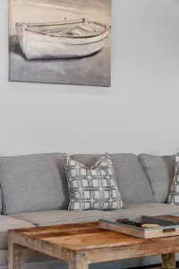 Relax in comfort on the large gray sectional! The seating area is accented with stylish pillows and overlooked by tranquil coastal artwork featuring a boat, perfect for unwinding after a day at the beach.