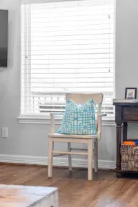 This bright corner of the living area features a charming white accent chair, beautifully dressed with a bright turquoise and white patterned pillow, adding a pop of color and coastal charm near the window.