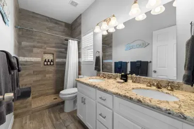 Indulge in this luxurious, spa-like master bathroom! It features a double vanity with granite counters, modern fixtures, and a shower beautifully tiled in wood-look planking. Fresh towels and stocked essentials  ensure a refreshing stay.