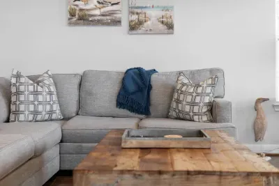 Relax in comfort on the large gray sectional! The seating area is accented with stylish pillows and overlooked by tranquil coastal artwork featuring a boat, perfect for unwinding after a day at the beach.