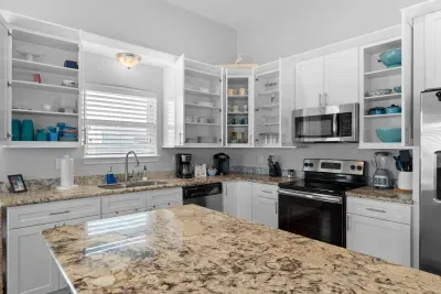 A bright, fully-stocked kitchen! White cabinets reveal dishes and glassware, ready for use. Enjoy granite counters and stainless steel appliances like the oven and microwave.