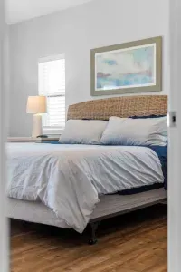 This inviting bed features a striking woven rattan headboard and calming coastal artwork. It is flanked by matching nightstands and lamps, ensuring a restful and stylish retreat.