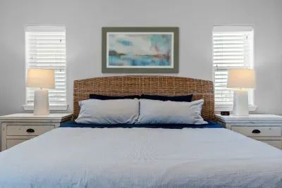 This inviting bed features a striking woven rattan headboard and calming coastal artwork. It is flanked by matching nightstands and lamps, ensuring a restful and stylish retreat.