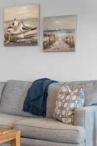 Relax in comfort on the large gray sectional! The seating area is accented with stylish pillows and overlooked by tranquil coastal artwork featuring a boat, perfect for unwinding after a day at the beach.