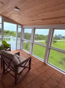 Take in the peaceful view from the glass-walled balcony, overlooking the lush yard, fruit trees, and the quiet road that leads to the beach, just a short stroll away.