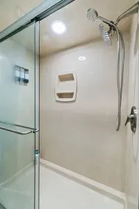 Clean lines and soft tones come together in this full bathroom, featuring warm brown cabinetry, marble tile accents, and a bright, refreshing atmosphere.