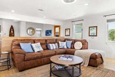 Cozy coastal retreat! Sink into the plush leather sectional with nautical pillows. Enjoy bright, natural light and easy access to the deck and kitchen. Relax and recharge here!