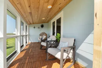 Take in the peaceful view from the glass-walled balcony, overlooking the lush yard, fruit trees, and the quiet road that leads to the beach, just a short stroll away.