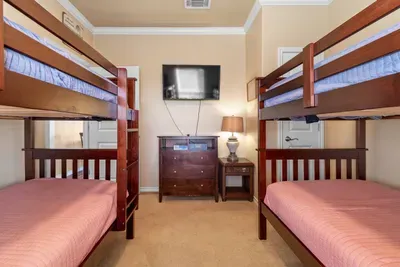 Fun bunk room perfect for kids or groups, featuring two sturdy bunk beds, a TV, dresser storage, and cozy lighting—great for movie nights and a good night’s sleep after the beach.