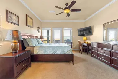 Large primary bedroom with a king bed, wall-mounted TV, and dresser space—plus deck access and relaxing coastal vibes for a comfortable stay.