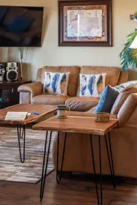 Unwind in the inviting living room with comfy leather seating, a large TV, and rustic wood tables—perfect for movie nights, morning coffee, or relaxing after a day of beach adventures.