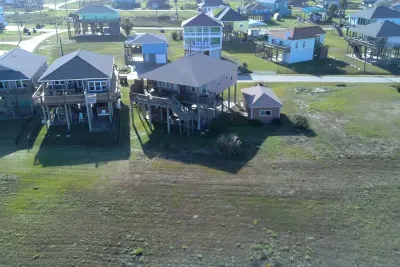 Aerial view of the home and neighborhood, with open space behind the property and the beach just a short walk away.