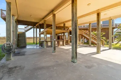 Huge covered space under the home with plenty of room to hang out, grill, and play—featuring a fun tiki bar setup and easy access to the stairs for quick trips up to the house.