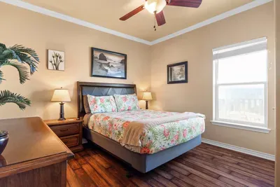 Bright, inviting bedroom with a cozy bed, warm bedside lamps, and coastal decor—plus plenty of natural light and relaxing views to help you unwind after a day at the beach.