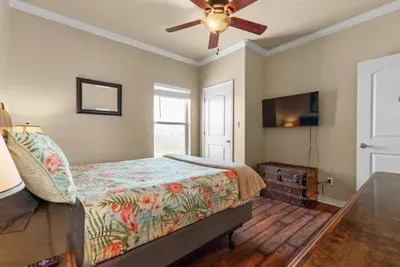 Comfortable, coastal-themed bedroom with a cozy bed, wall-mounted TV, and plenty of natural light—perfect for relaxing and recharging after a day at the beach.