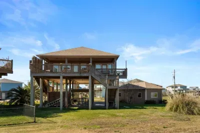 Exterior view of the home with a spacious wraparound deck, elevated coastal design, and plenty of room to relax and enjoy the beach breeze.