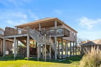 Bright coastal exterior with a large deck, easy stair access, and shaded space underneath—perfect for relaxing after a day at the beach.