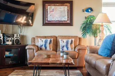 Cozy sitting area with comfy leather seating, a large TV, and a coffee table—perfect for movie nights, relaxing with a drink, or hanging out after a fun day at the beach.